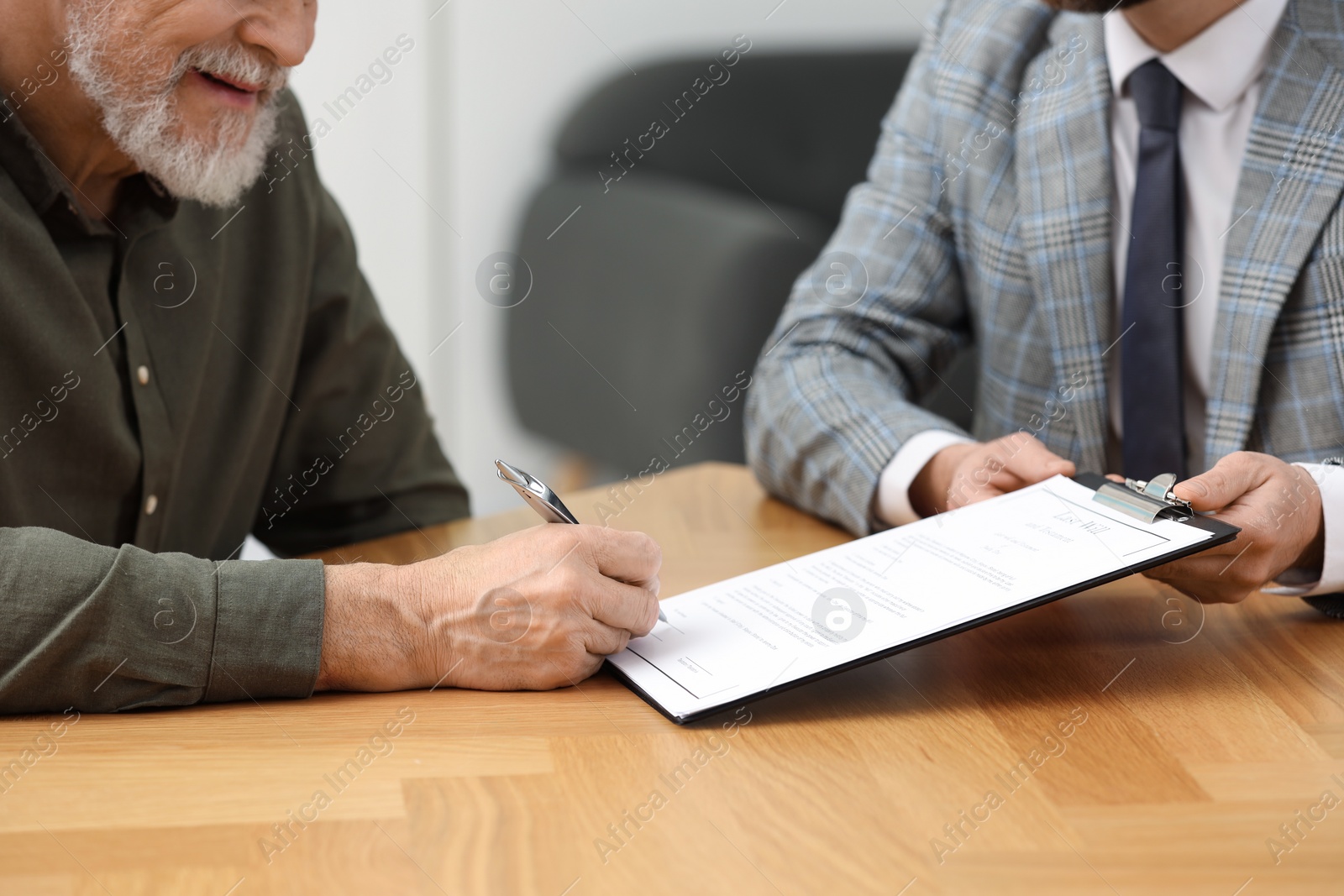 Photo of Notary showing senior man where to sign Last Will and Testament at wooden table indoors, closeup