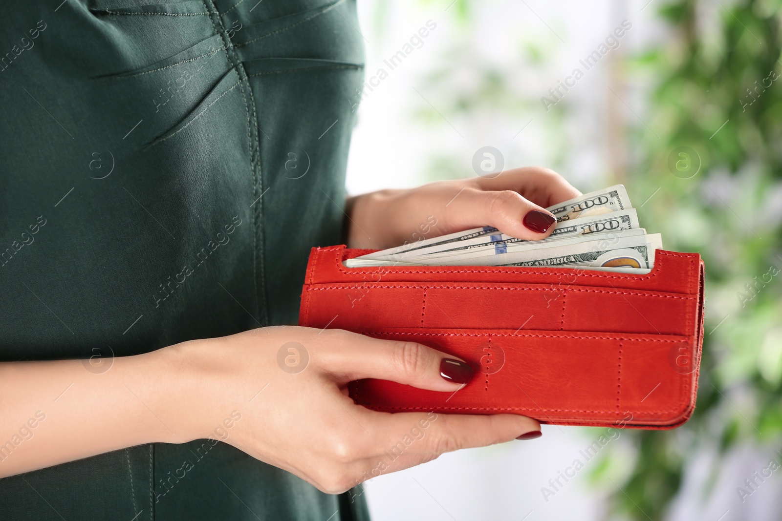 Photo of Woman putting money into wallet on blurred background, closeup