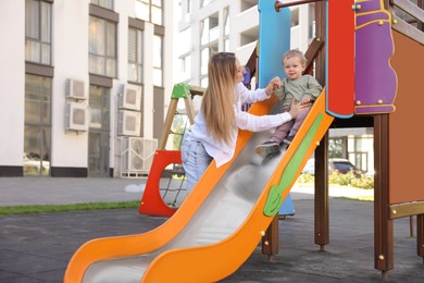 Happy nanny and cute little boy on slide outdoors