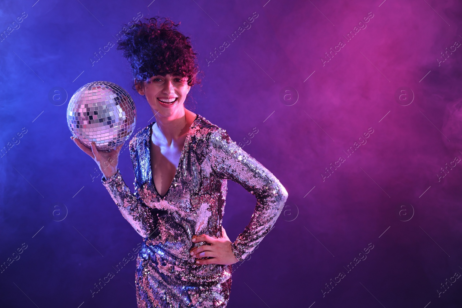 Photo of Beautiful young woman with disco ball posing on color background in neon lights. Space for text