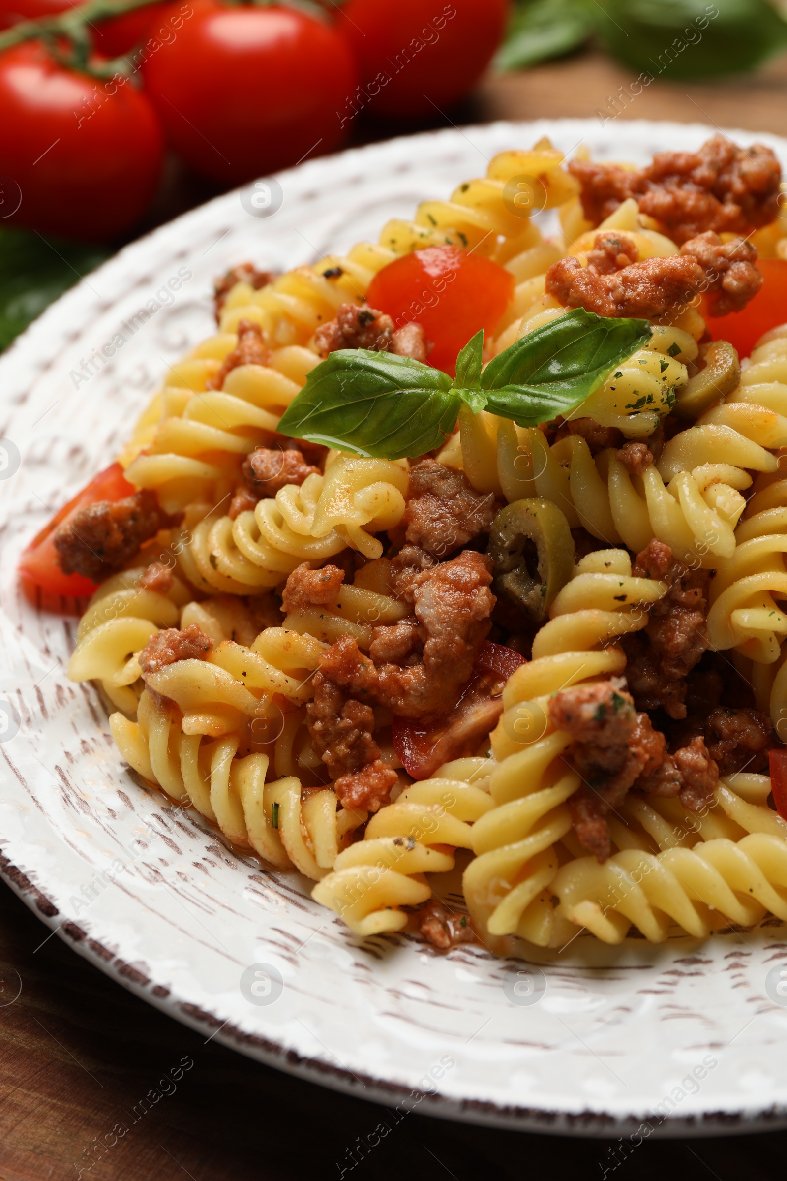 Photo of Plate of delicious pasta with minced meat, tomatoes and basil on table, closeup