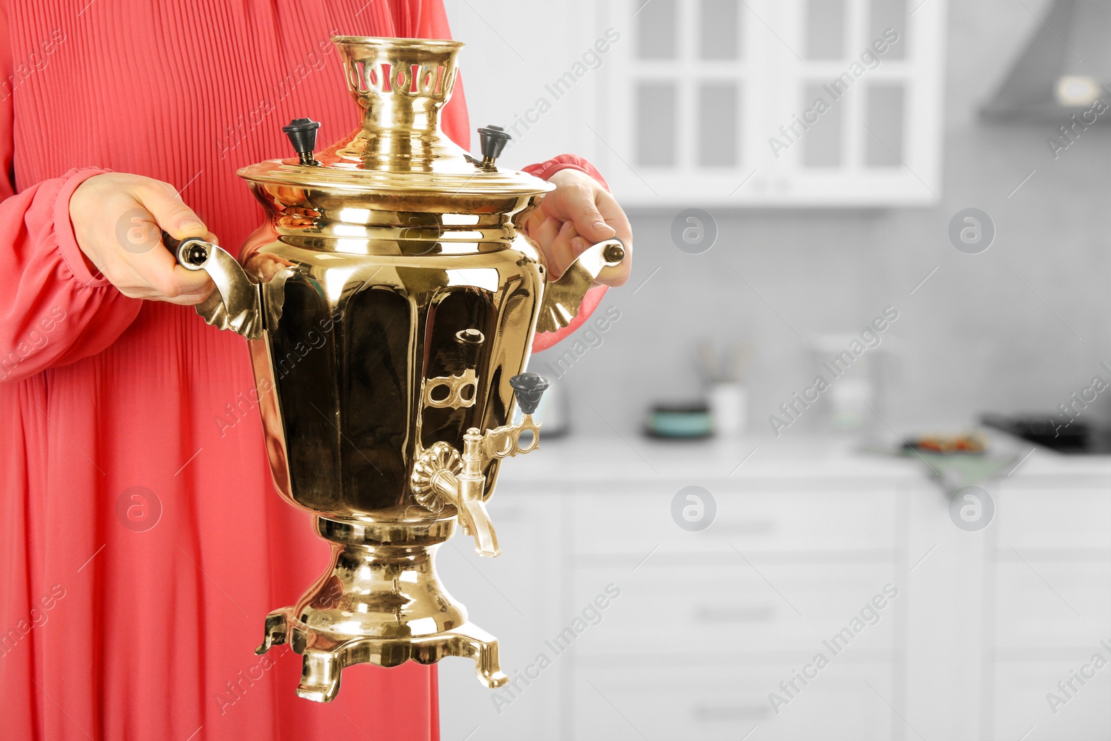 Image of Woman holding traditional Russian samovar in kitchen, closeup. Space for text