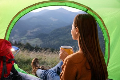Photo of Young woman with drink inside of camping tent in mountains