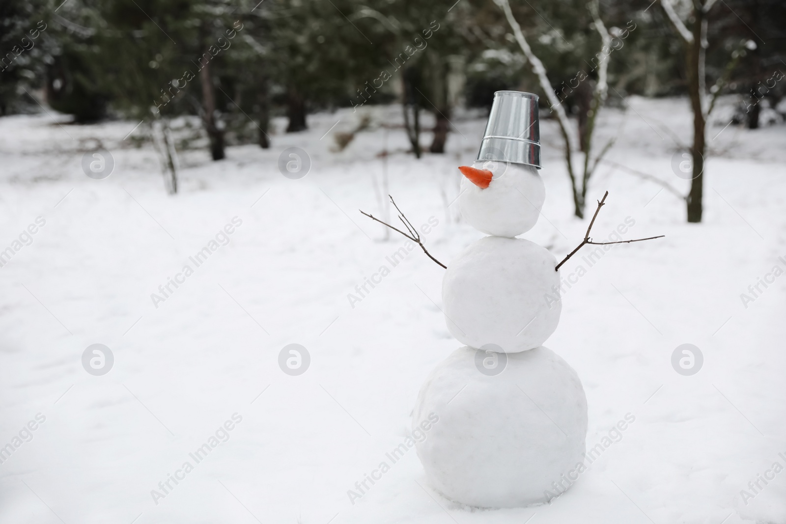 Photo of Cute snowman with metal bucket and carrot nose outdoors on winter day, space for text