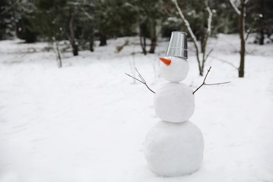 Cute snowman with metal bucket and carrot nose outdoors on winter day, space for text