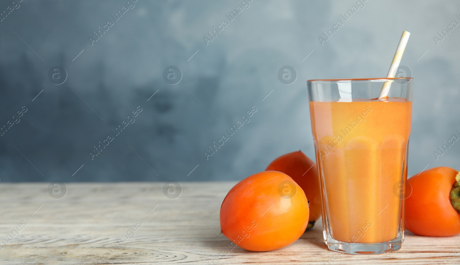 Photo of Tasty persimmon smoothie and fresh fruits on white wooden table against light blue background. Space for text