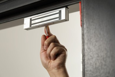Photo of Man with screwdriver installing electromagnetic door lock indoors, closeup. Home security