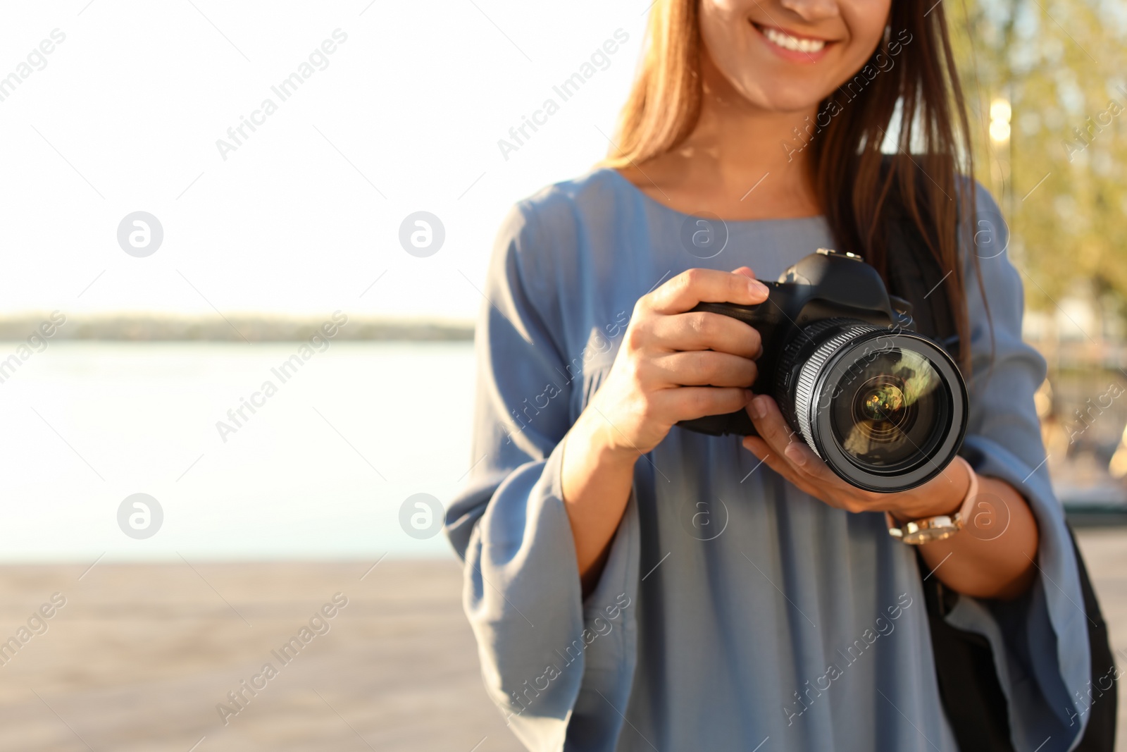 Photo of Young female photographer holding professional camera at pier. Space for text