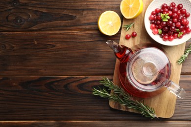 Photo of Tasty hot cranberry tea, lemon, rosemary and fresh berries on wooden table