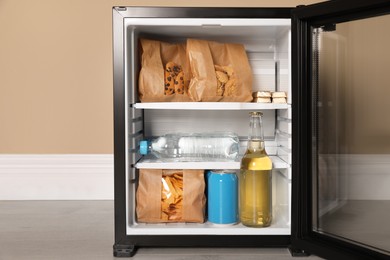 Mini bar filled with food and drinks near beige wall indoors, closeup