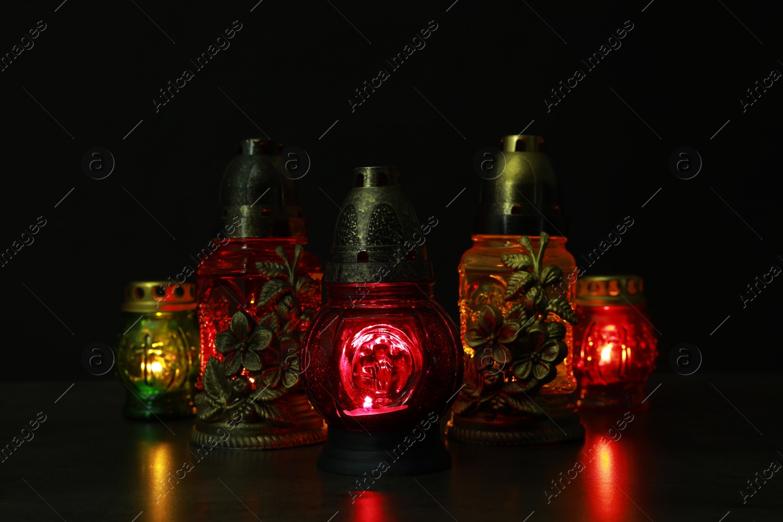 Photo of Beautiful glowing grave lights on table in darkness. Symbol of remembrance