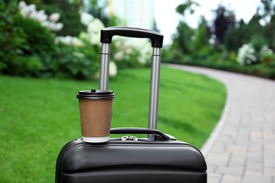 Photo of Paper cup of hot coffee on suitcase outdoors. Takeaway drink