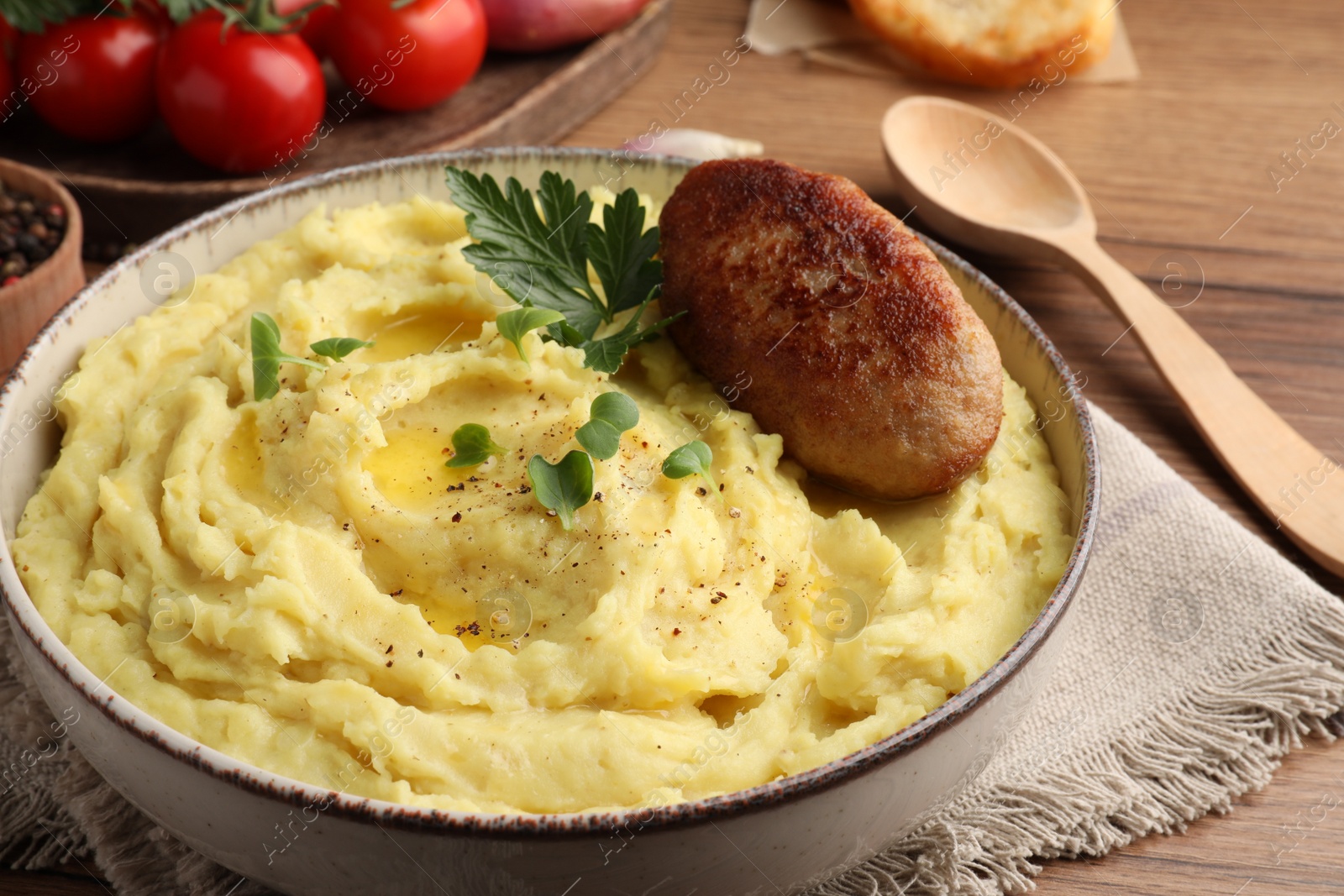 Photo of Bowl of tasty mashed potatoes with parsley, black pepper and cutlet served on wooden table, closeup