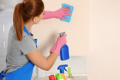 Woman in protective gloves cleaning kitchen with rag, indoors