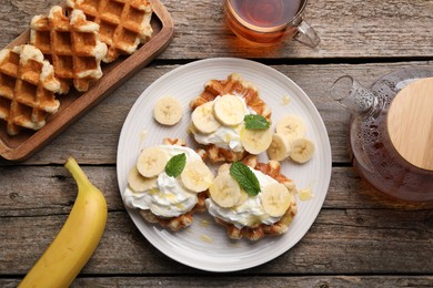 Photo of Delicious Belgian waffles with banana and whipped cream served on wooden table, flat lay