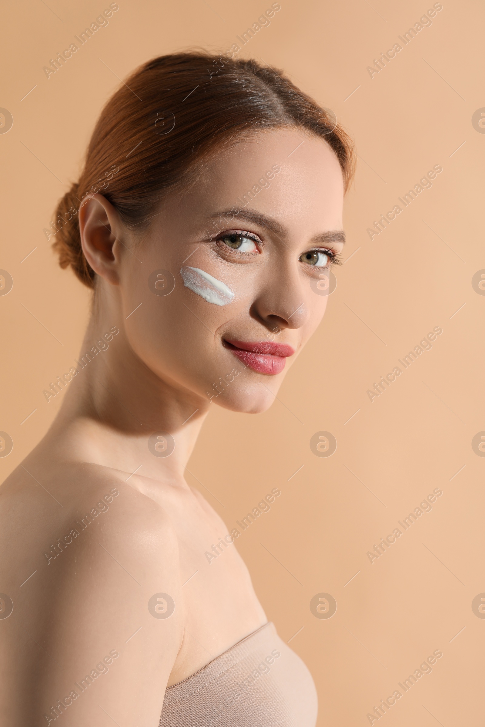 Photo of Beautiful young woman with sun protection cream on her face against beige background