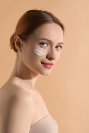 Beautiful young woman with sun protection cream on her face against beige background