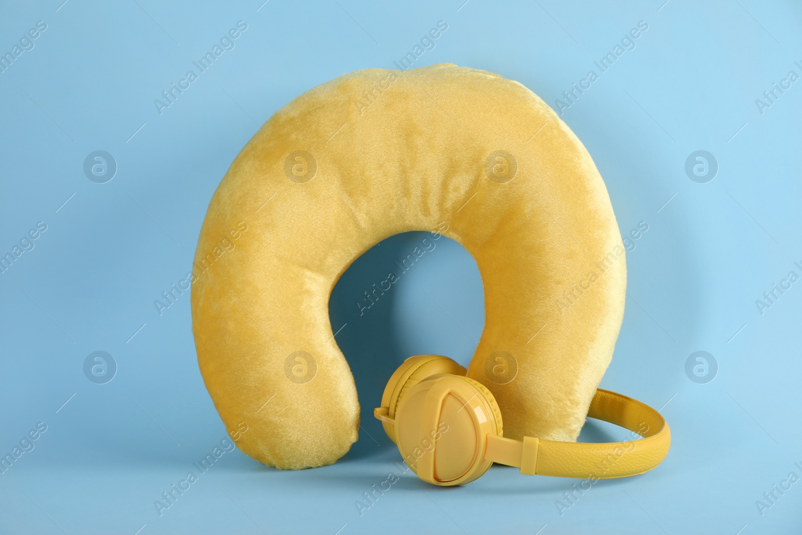 Photo of Yellow travel pillow and headphones on light blue background