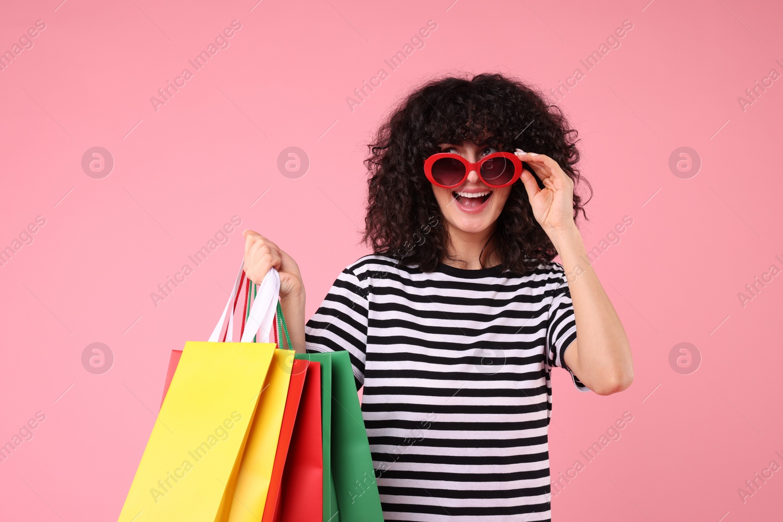 Photo of Happy young woman with shopping bags and stylish sunglasses on pink background