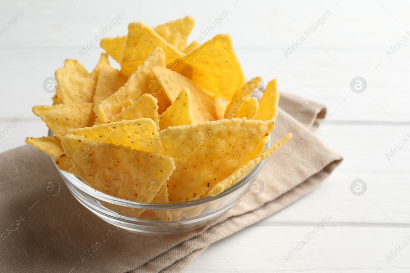 Photo of Tortilla chips (nachos) in bowl on white wooden table, closeup