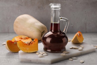 Photo of Fresh pumpkin seed oil in glass jug on grey table