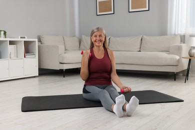 Senior woman exercising with dumbbells on mat at home. Sports equipment