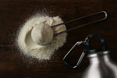 Photo of Measuring scoop of protein powder and bottle on wooden table, flat lay