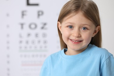 Photo of Cute little girl against vision test chart