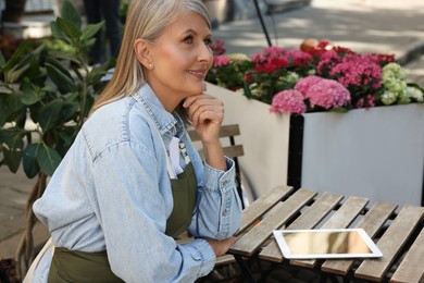 Photo of Happy business owner with tablet at table near her flower shop outdoors