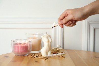 Woman lighting female body shaped candle on wooden table, closeup. Stylish decor