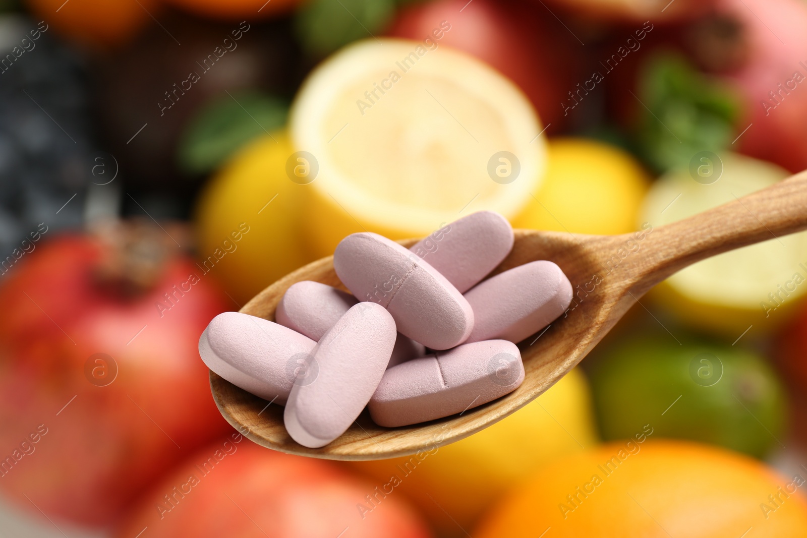 Photo of Vitamin pills in spoon against fresh fruits, closeup