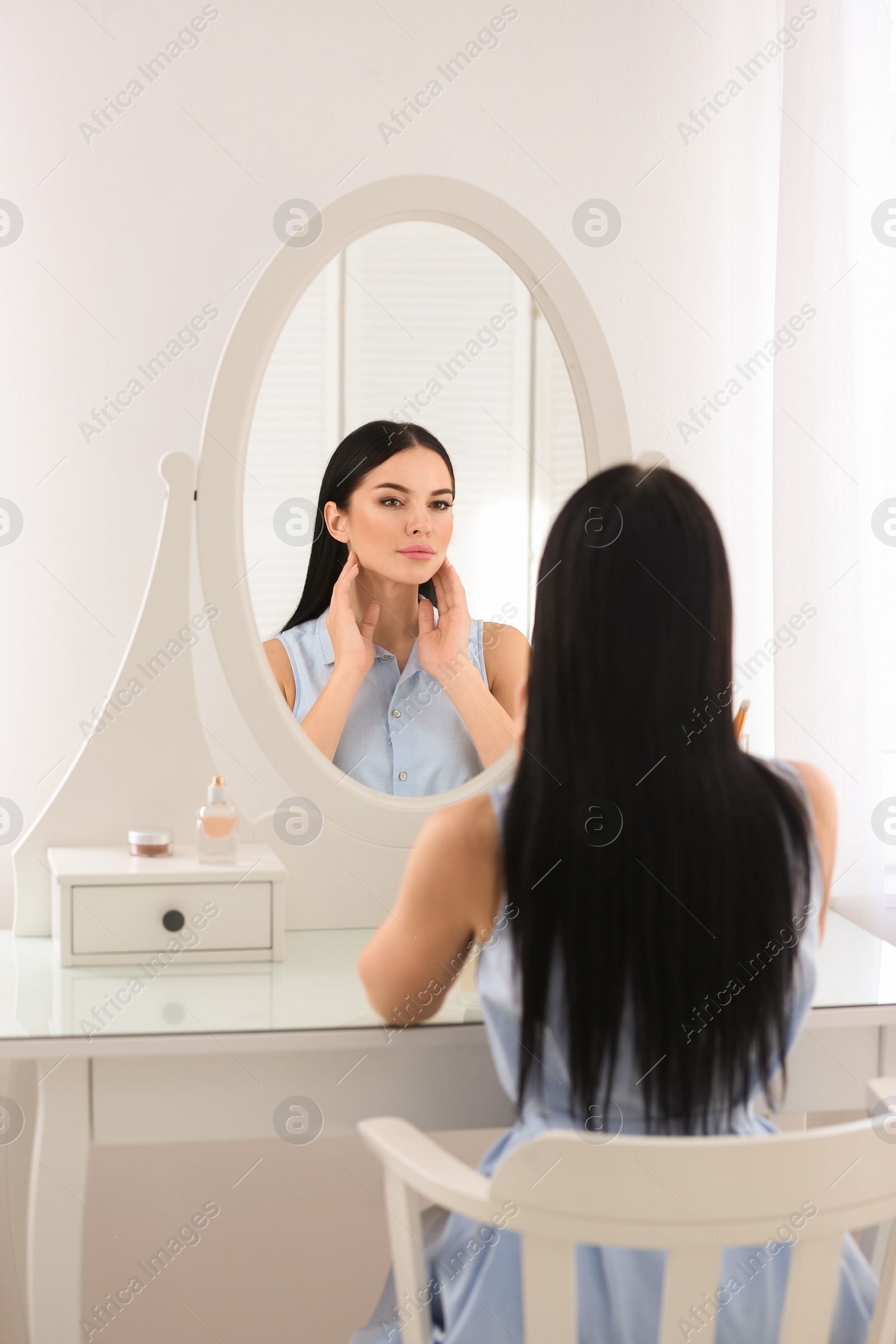 Photo of Beautiful young woman looking at herself in mirror indoors