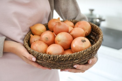 Photo of Woman holding basket with golden onions on blurred background, closeup