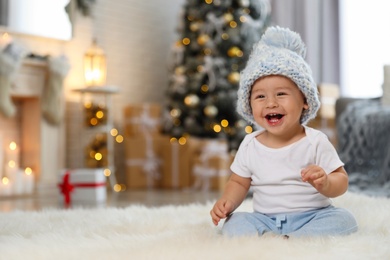 Photo of Little baby wearing knitted hat on floor at home. First Christmas