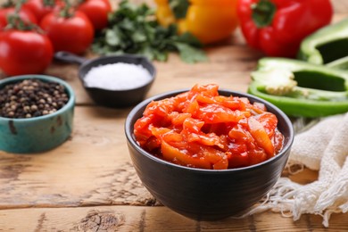 Bowl of delicious lecho and ingredients on wooden table, closeup. Space for text