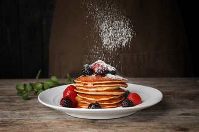 Photo of Delicious pancakes with berries and powdered sugar served for breakfast on table