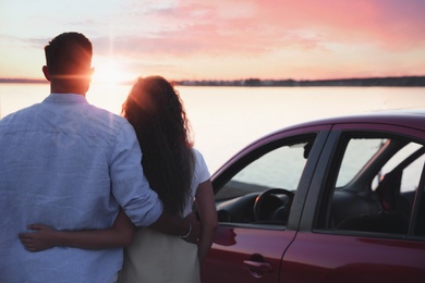Photo of Couple near car outdoors at sunset, back view. Summer trip