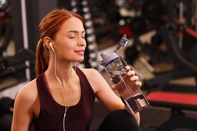 Photo of Beautiful young woman with earphones and bottle of water in gym