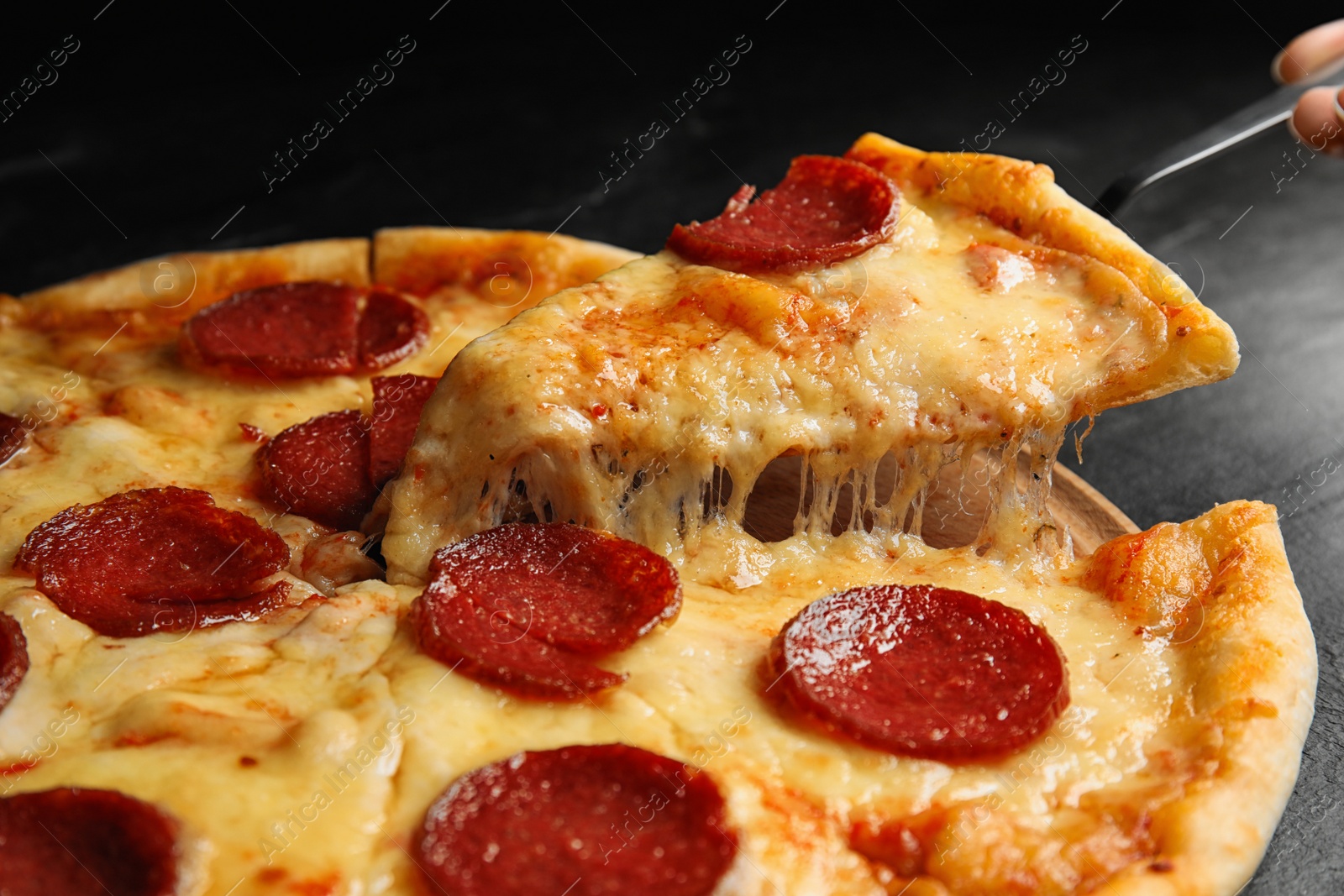 Photo of Taking slice of tasty pepperoni pizza on black table, closeup