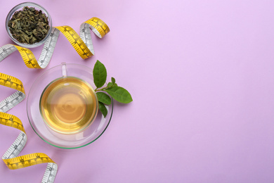 Photo of Flat lay composition with glass cup of diet herbal tea and measuring tape on violet background, space for text