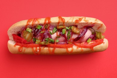 Tasty hot dog with onion, tomato, pickles and sauce on red background, top view