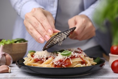 Photo of Woman grating parmesan cheese onto delicious pasta at wooden table, closeup