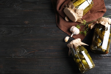 Photo of Flat lay composition with jars of pickled cucumbers on black wooden table, space for text