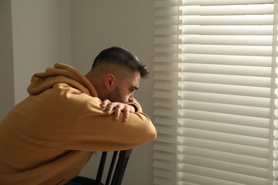 Sad man sitting on chair near window. Space for text