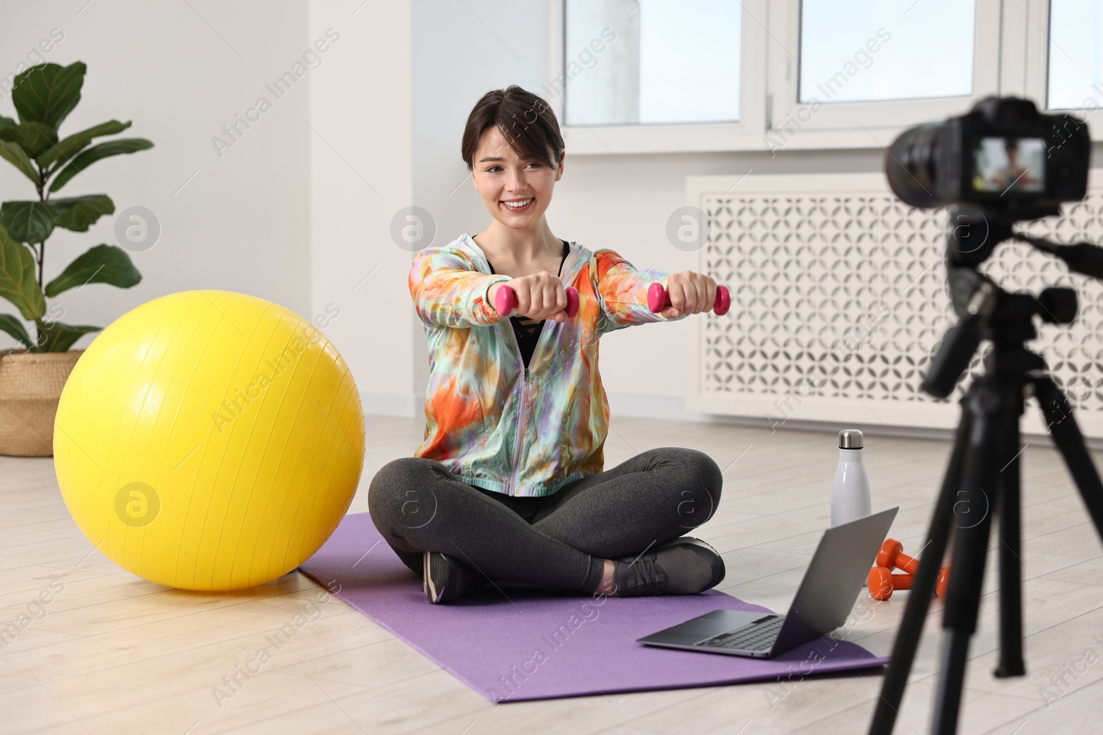 Photo of Happy sports blogger training with dumbbells while recording fitness lesson at home