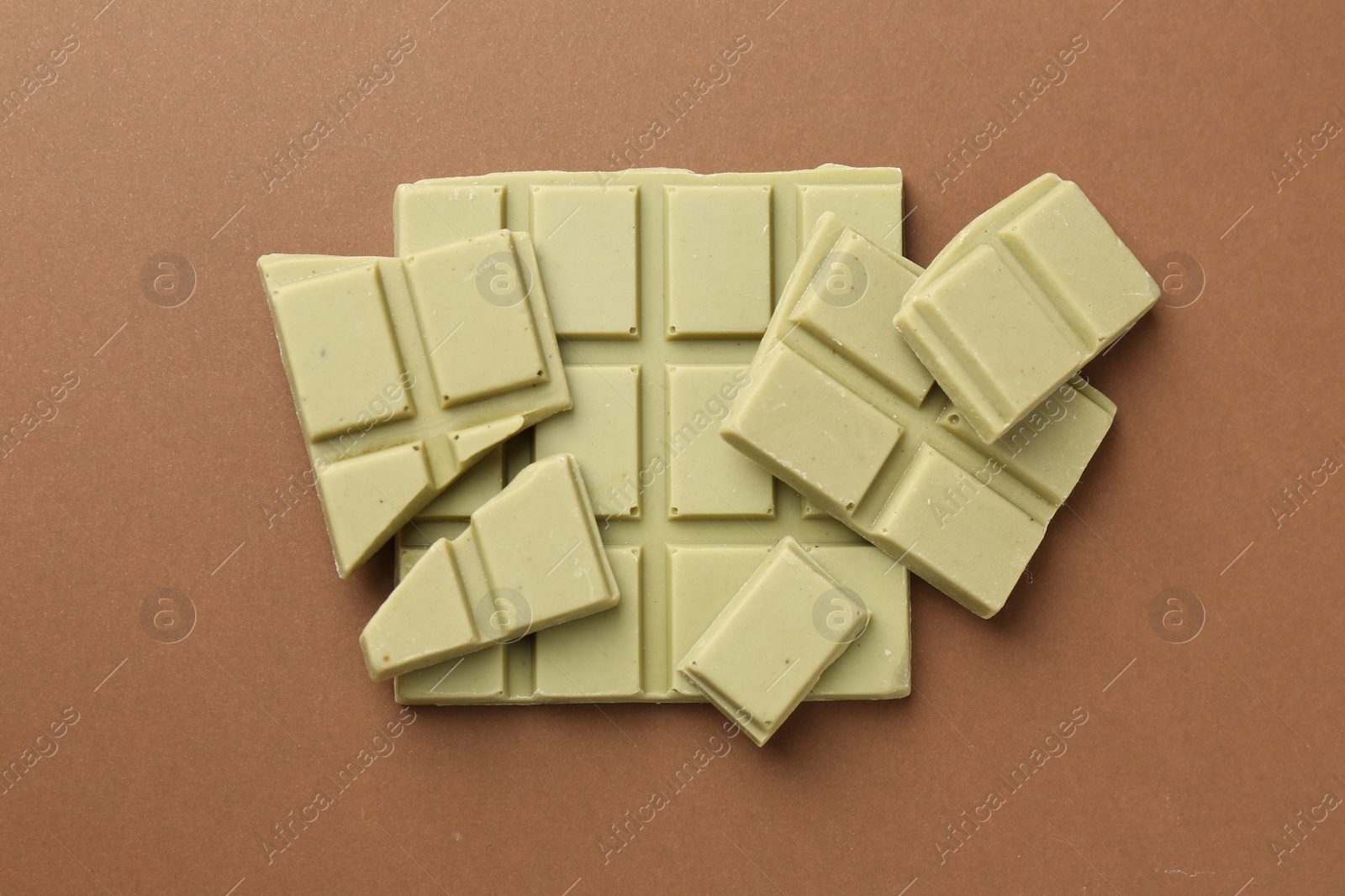 Photo of Pieces of tasty matcha chocolate bar on brown background, top view
