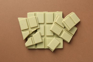 Pieces of tasty matcha chocolate bar on brown background, top view