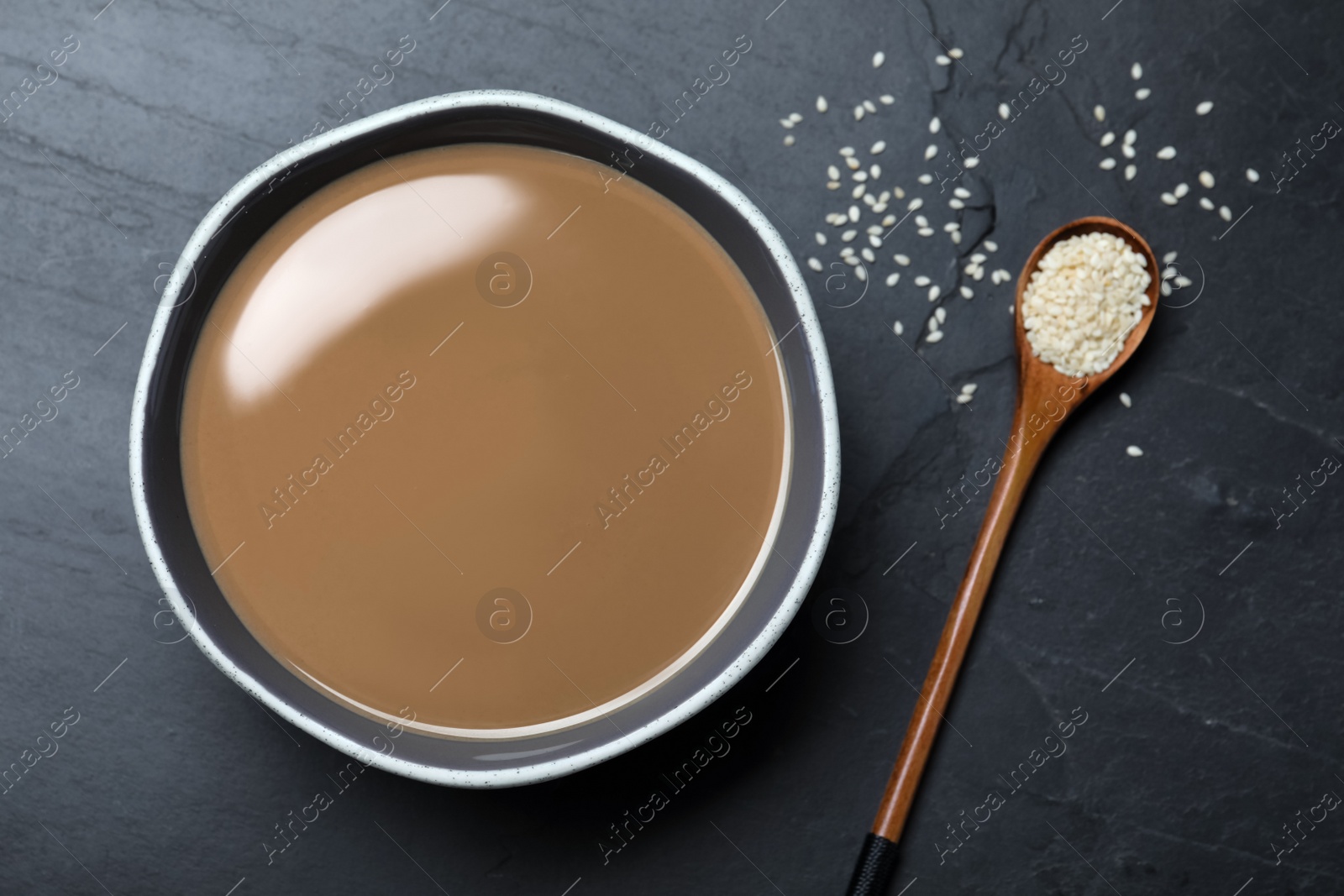 Photo of Tasty sesame paste, spoon and seeds on black table, flat lay