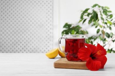 Photo of Delicious hibiscus tea and beautiful flower on white wooden table, space for text