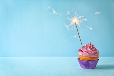 Photo of Delicious birthday cupcake with sparkler on color background